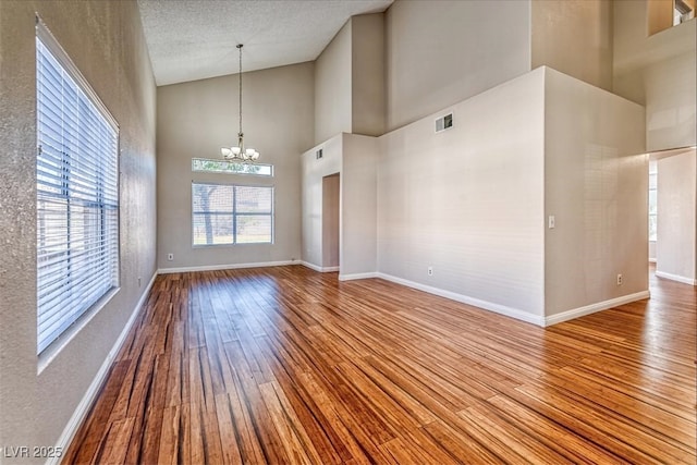 interior space featuring baseboards, an inviting chandelier, visible vents, high vaulted ceiling, and wood finished floors