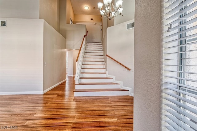 stairway featuring visible vents, baseboards, a notable chandelier, a high ceiling, and wood finished floors