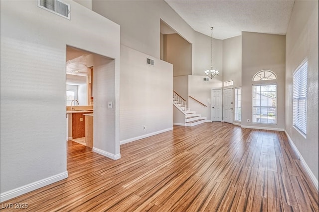 unfurnished living room with wood finished floors, high vaulted ceiling, baseboards, and visible vents