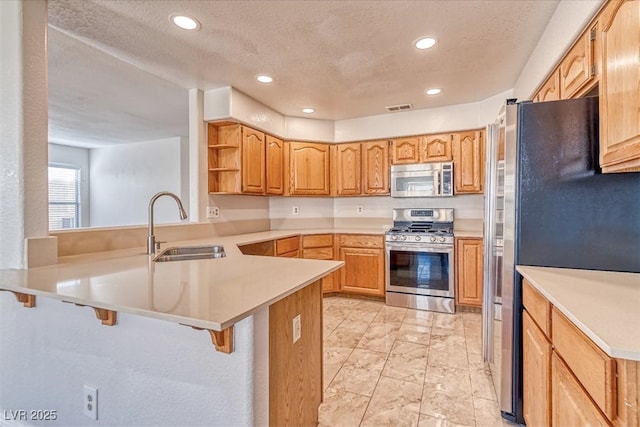 kitchen featuring visible vents, a sink, appliances with stainless steel finishes, a kitchen bar, and a peninsula