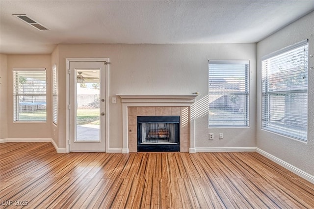 unfurnished living room featuring baseboards, wood finished floors, a tiled fireplace, and visible vents