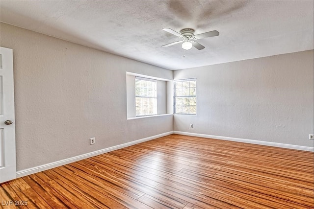 empty room with wood-type flooring, baseboards, a ceiling fan, and a textured wall