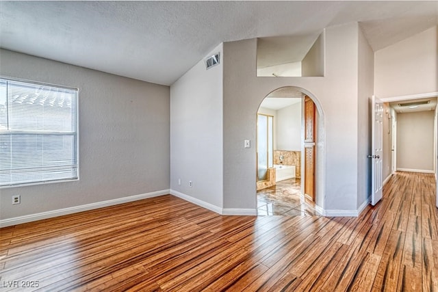 unfurnished room with visible vents, baseboards, arched walkways, a textured ceiling, and wood finished floors