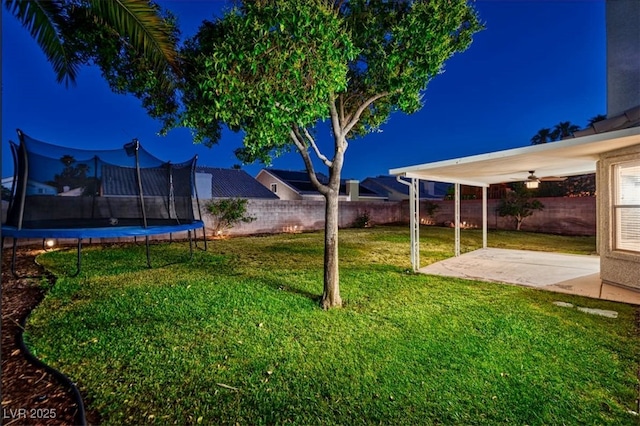 yard at twilight featuring a fenced backyard, a trampoline, and a patio