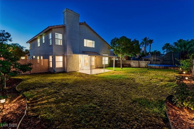 rear view of property featuring a trampoline, a patio, stucco siding, a fenced backyard, and a lawn