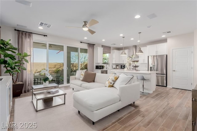 living room featuring a ceiling fan, light wood finished floors, visible vents, and recessed lighting