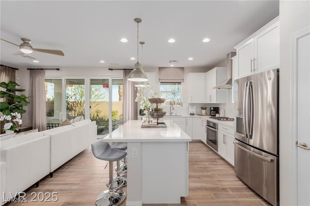 kitchen with light wood-type flooring, open floor plan, extractor fan, light countertops, and appliances with stainless steel finishes
