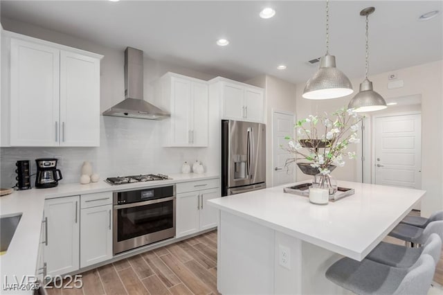 kitchen with wall chimney range hood, tasteful backsplash, a kitchen bar, appliances with stainless steel finishes, and a kitchen island