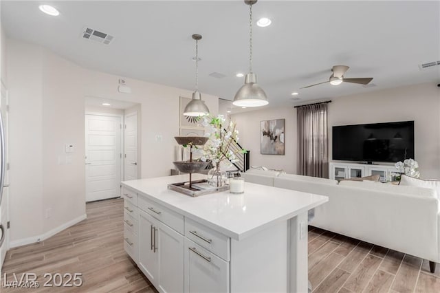 kitchen with white cabinets, visible vents, a ceiling fan, light wood-style floors, and open floor plan