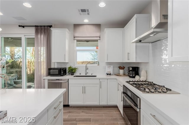 kitchen with wall chimney exhaust hood, stainless steel appliances, a sink, visible vents, and light countertops