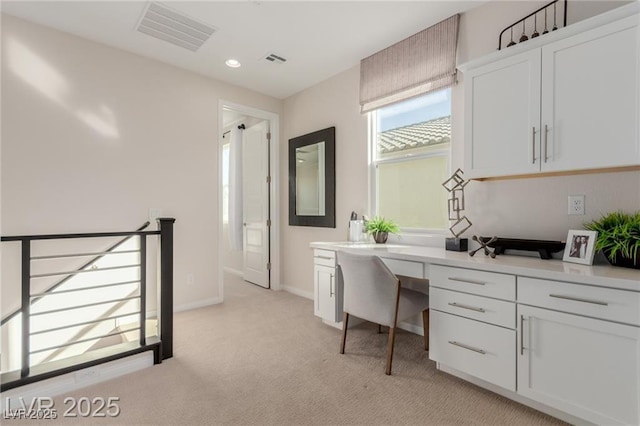 office area with baseboards, visible vents, built in desk, and light colored carpet