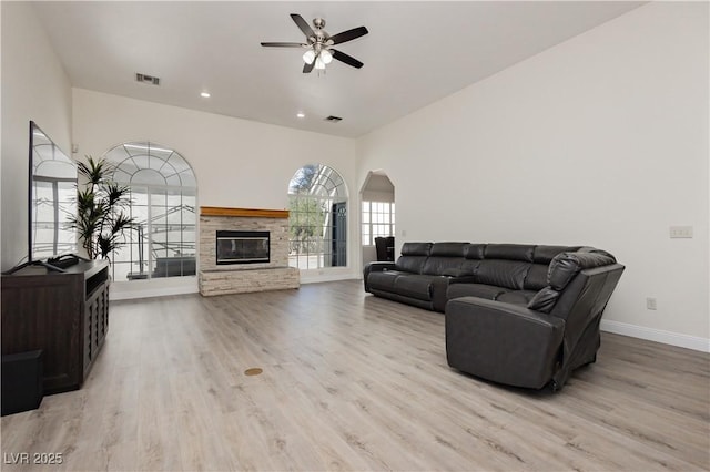 living room featuring visible vents, baseboards, a ceiling fan, a fireplace, and light wood finished floors