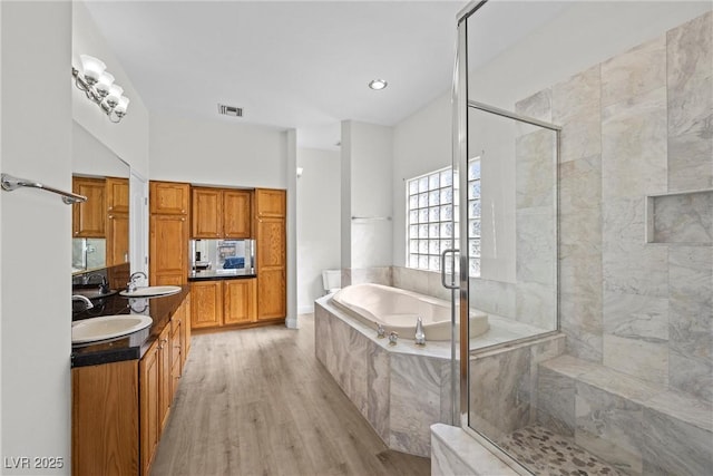 bathroom with double vanity, a stall shower, visible vents, a bath, and wood finished floors