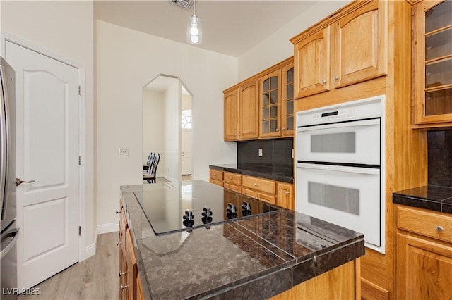 kitchen with light wood-type flooring, black electric stovetop, a kitchen island, arched walkways, and double oven