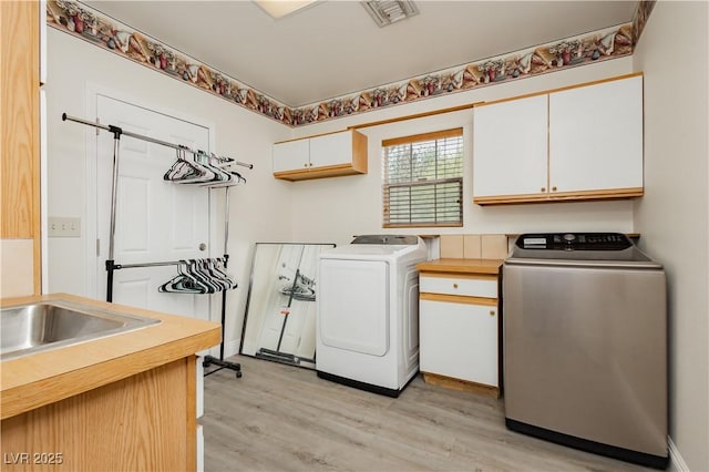 clothes washing area featuring light wood-style floors, independent washer and dryer, visible vents, and cabinet space