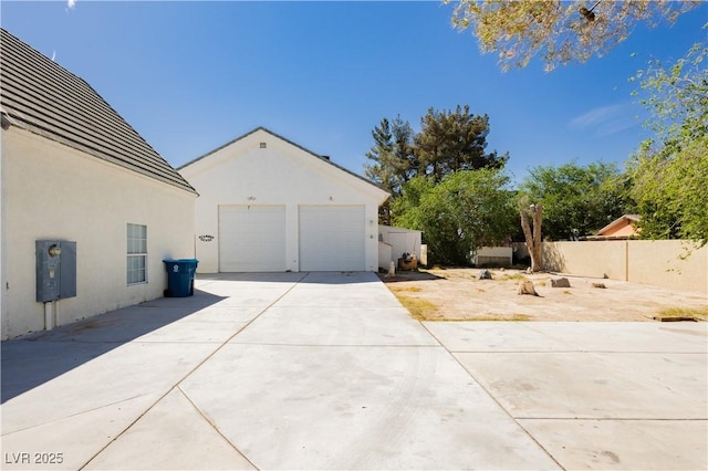 view of side of home featuring a garage, stucco siding, fence, and an outdoor structure