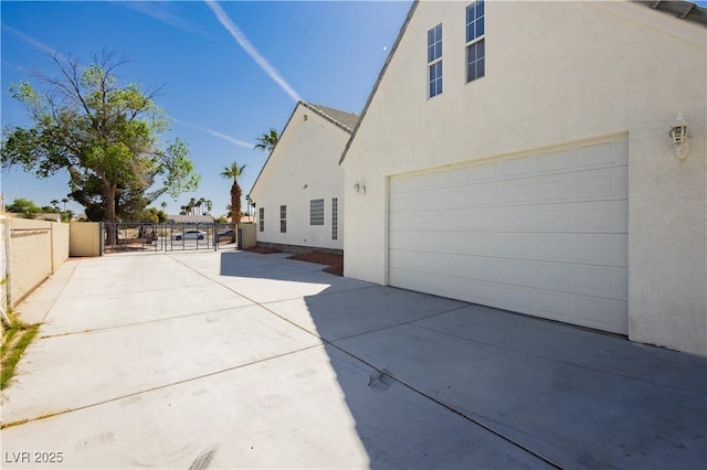 view of home's exterior with an attached garage, fence, driveway, and stucco siding