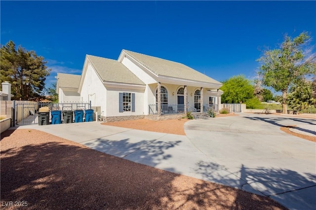 view of front of house with concrete driveway, a porch, stucco siding, and fence