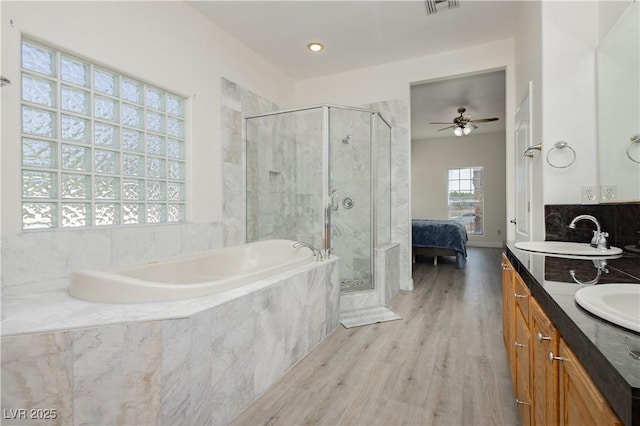 ensuite bathroom with a ceiling fan, a shower stall, a bath, a sink, and wood finished floors