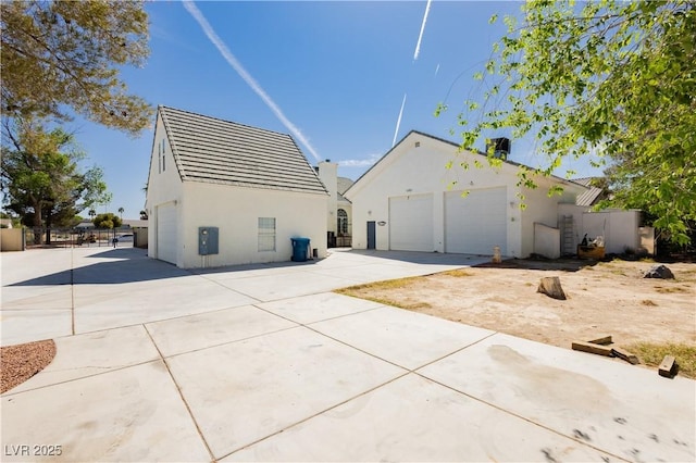 rear view of house featuring stucco siding, an outdoor structure, fence, and a detached garage