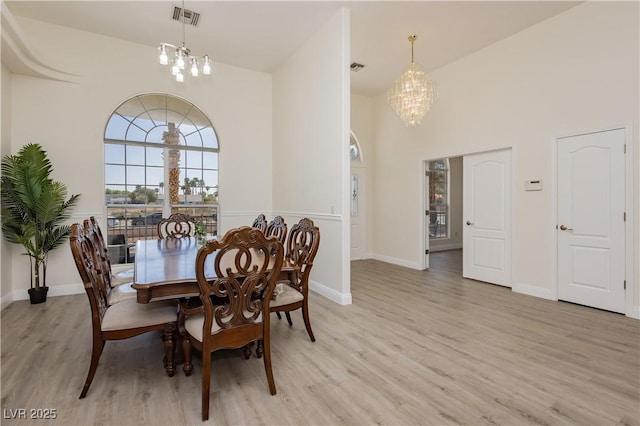 dining area featuring baseboards, an inviting chandelier, light wood-style flooring, a high ceiling, and visible vents