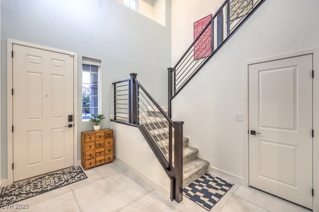tiled entrance foyer featuring baseboards, a towering ceiling, and stairway