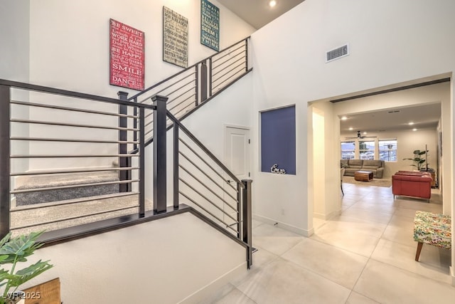 stairway with a towering ceiling, baseboards, visible vents, tile patterned flooring, and ceiling fan