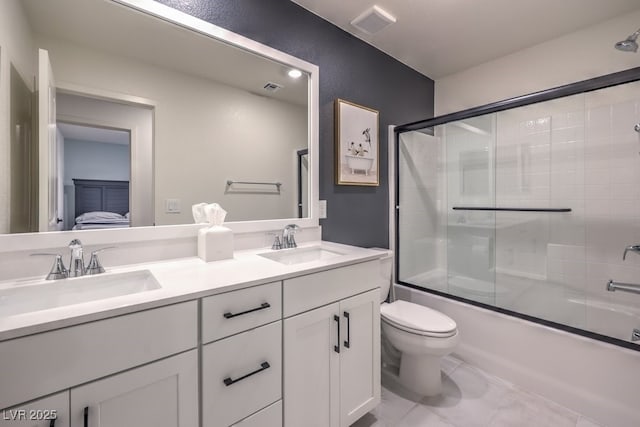 bathroom featuring toilet, enclosed tub / shower combo, double vanity, and a sink
