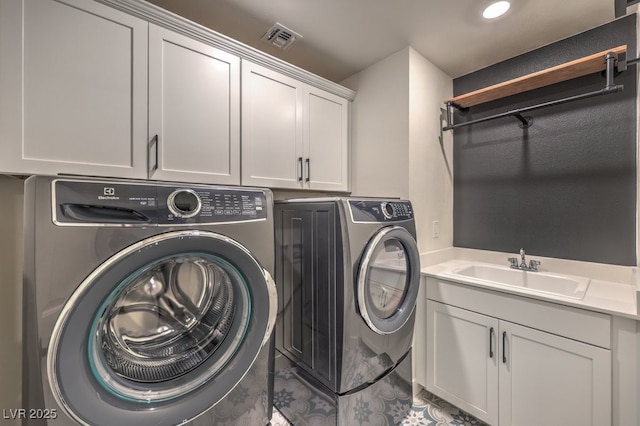 washroom featuring washing machine and dryer, visible vents, cabinet space, and a sink