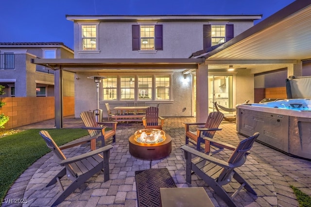 back of property with a hot tub, an outdoor fire pit, fence, a patio, and stucco siding