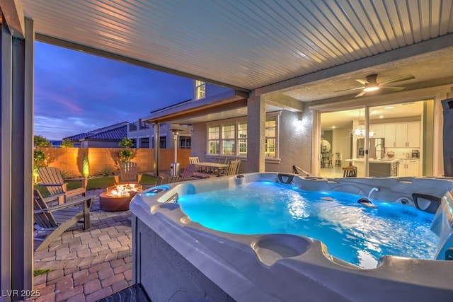 pool at dusk with a fire pit, a hot tub, a patio area, ceiling fan, and fence
