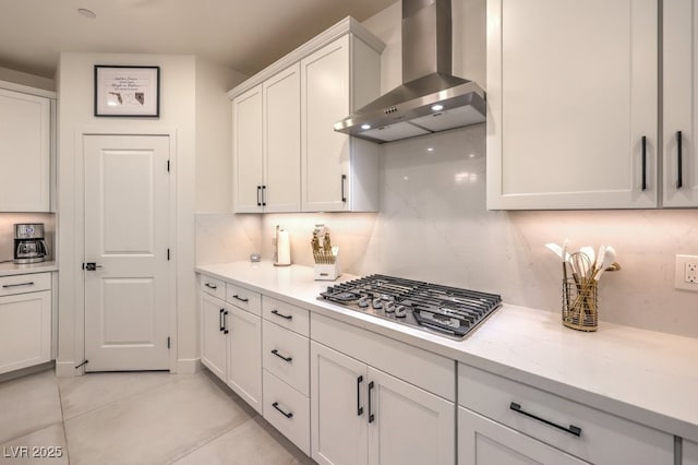 kitchen with light tile patterned floors, wall chimney exhaust hood, decorative backsplash, stainless steel gas cooktop, and white cabinetry