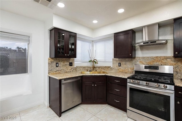 kitchen featuring wall chimney exhaust hood, dark brown cabinetry, a sink, stainless steel appliances, and decorative backsplash