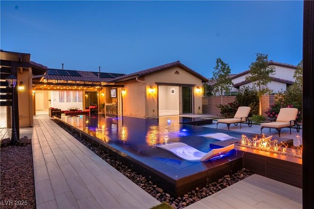 exterior space with roof mounted solar panels, stucco siding, an outdoor fire pit, and a patio area