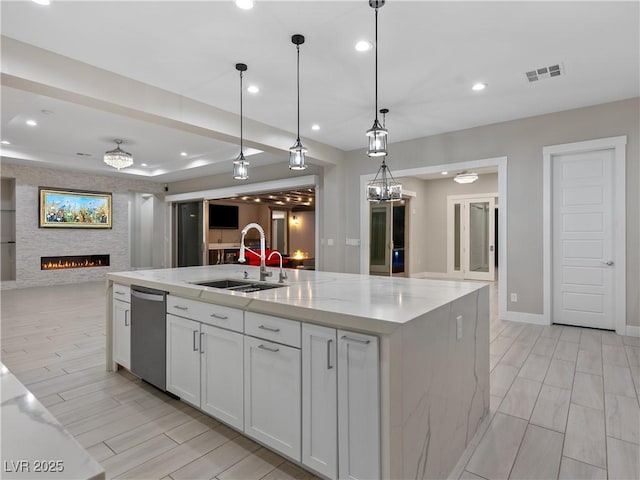 kitchen with visible vents, stainless steel dishwasher, open floor plan, white cabinets, and a sink