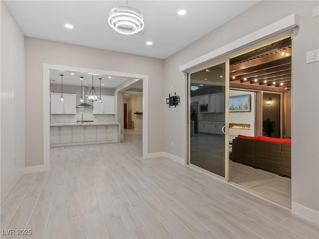 interior space featuring baseboards, a lit fireplace, an inviting chandelier, and light wood-type flooring