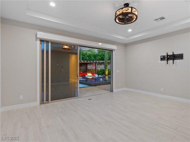 spare room with recessed lighting, wood finished floors, a tray ceiling, and visible vents