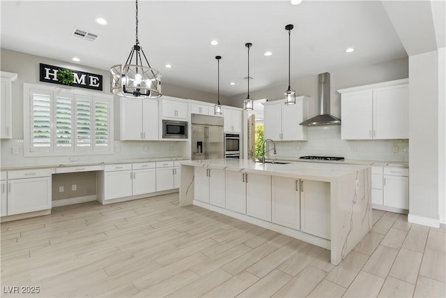 kitchen featuring visible vents, decorative backsplash, built in appliances, wall chimney exhaust hood, and a sink