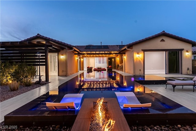 back of house featuring stucco siding, an outdoor pool, solar panels, a tiled roof, and a fire pit