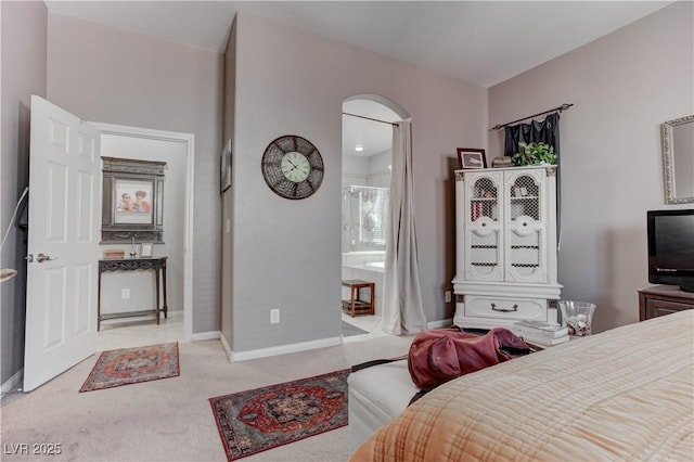 bedroom with carpet floors, ensuite bathroom, baseboards, and arched walkways