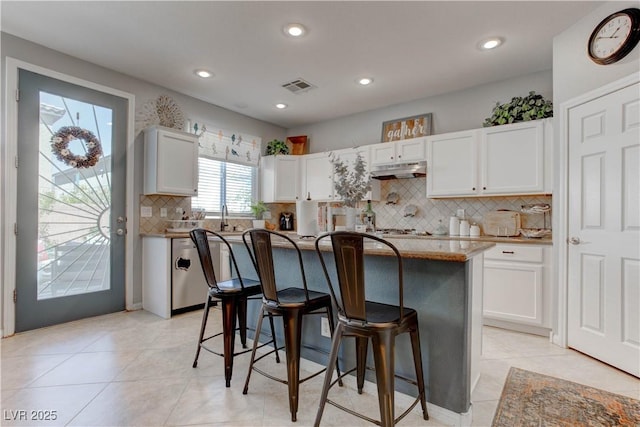 kitchen featuring a kitchen breakfast bar, visible vents, white cabinets, and under cabinet range hood