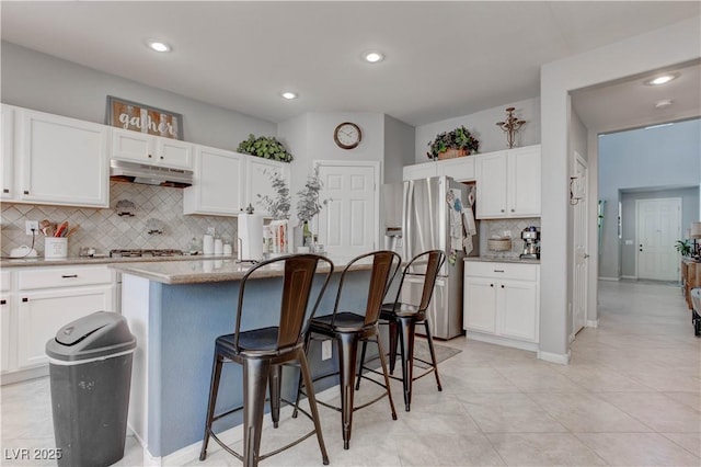 kitchen featuring stainless steel fridge, white cabinetry, decorative backsplash, and under cabinet range hood