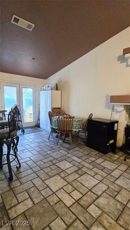 dining space with visible vents, brick floor, lofted ceiling, and french doors