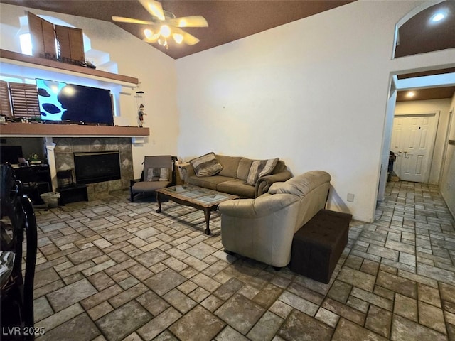 living area featuring ceiling fan, a fireplace, brick floor, and lofted ceiling