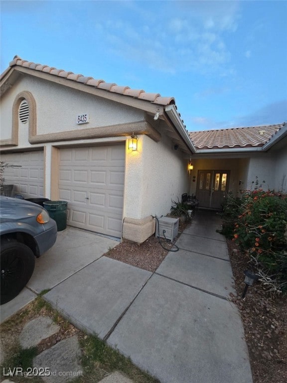 view of side of home with a garage, stucco siding, driveway, and a tile roof
