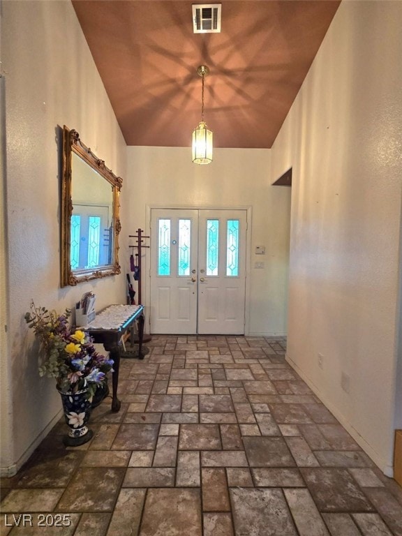 entrance foyer with high vaulted ceiling, visible vents, and brick floor