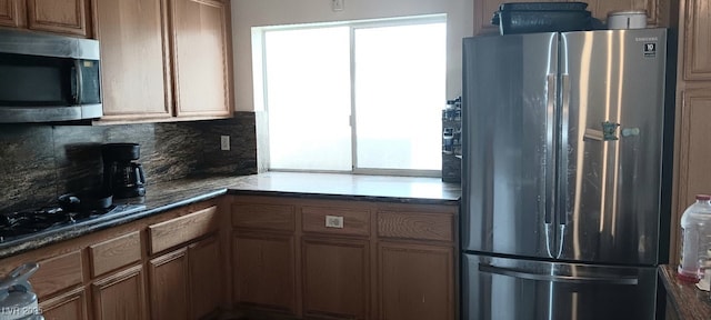 kitchen featuring decorative backsplash, appliances with stainless steel finishes, brown cabinets, and dark countertops