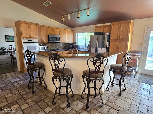 kitchen featuring decorative backsplash, a kitchen island with sink, a breakfast bar area, visible vents, and appliances with stainless steel finishes
