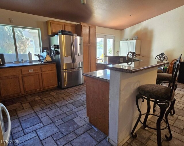 kitchen with stainless steel fridge, brown cabinets, and dark countertops