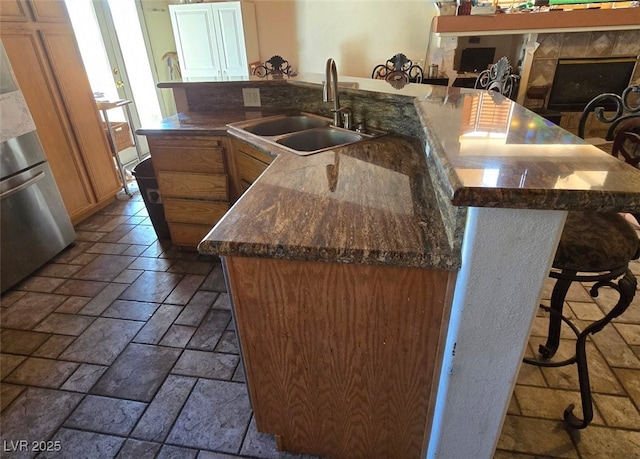 kitchen with fridge, a breakfast bar, a sink, stone tile floors, and a large island with sink